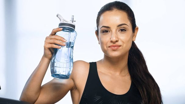молодая спортивная женщина держит спортивную бутылку с водой в тренажерном зале  - Фото, изображение