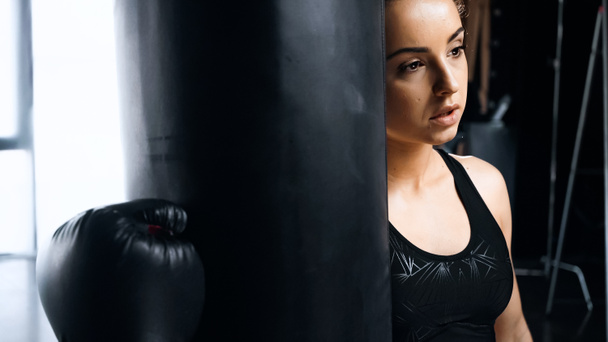 tired sportswoman in boxing glove leaning on punching bag - Fotografie, Obrázek