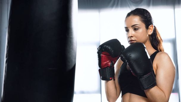 bokszkesztyűs és sportszerkós nő bokszzsákkal tornázik az edzőteremben - Fotó, kép