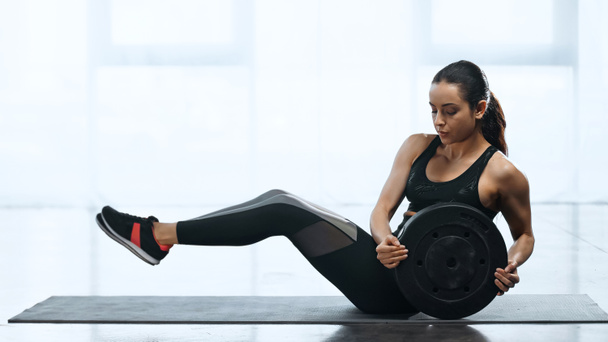 young sportswoman working out with weight plate on fitness mat in gym - Photo, Image