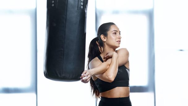 young sportswoman stretching near punching bag - Фото, изображение