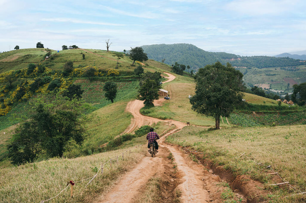 Homem de bicicleta motocicleta velha na estrada de cascalho até a colina verde no campo - Foto, Imagem