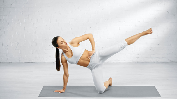 Frau in Sportbekleidung mit Hand an der Hüfte praktiziert Yoga zu Hause  - Foto, Bild