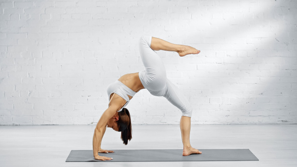Vista lateral de la mujer descalza en pose de arco hacia arriba en la esterilla de yoga en casa  - Foto, imagen