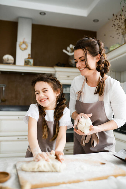 Happy mom and daughter in aprons are cooking in the kitchen preparing raw dough for cookies - Fotó, kép