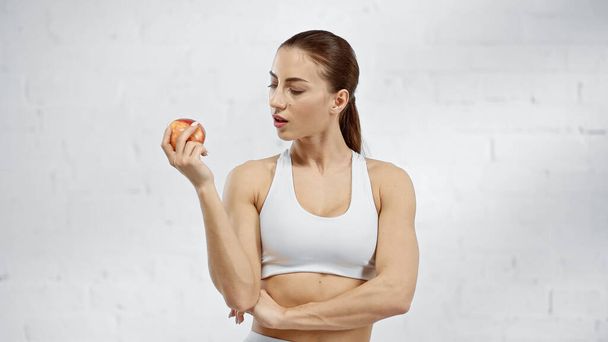 Woman in white sports top looking at red apple  - Foto, imagen