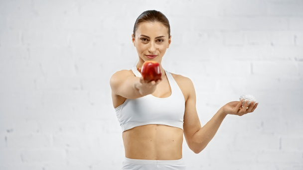 Sportswoman holding marshmallow and blurred apple  - Photo, Image