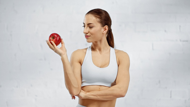 Sportswoman in white sports top looking at ripe apple  - Fotografie, Obrázek