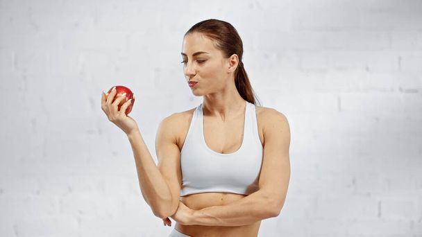 Fit sportswoman looking at fresh apple at home  - Foto, imagen
