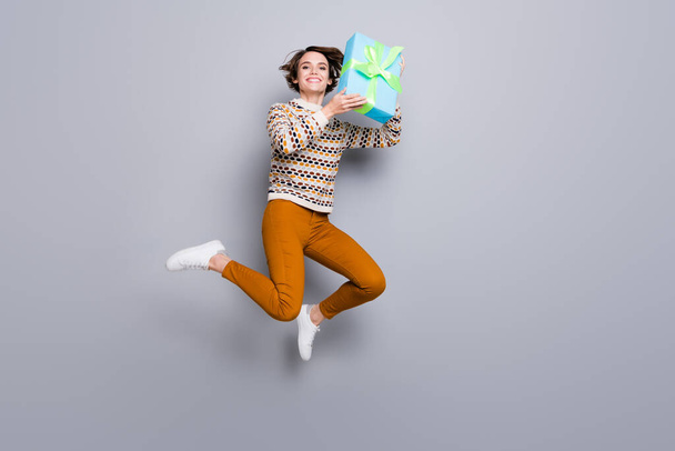 Tamanho do corpo de comprimento total vista de menina alegre agradável pulando segurando em mãos giftbox isolado sobre fundo de cor pastel cinza - Foto, Imagem