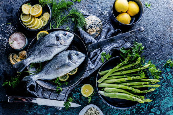 top view of fresh healthy sea bream fish with asparagus, lemon and spices over dark background - Фото, зображення