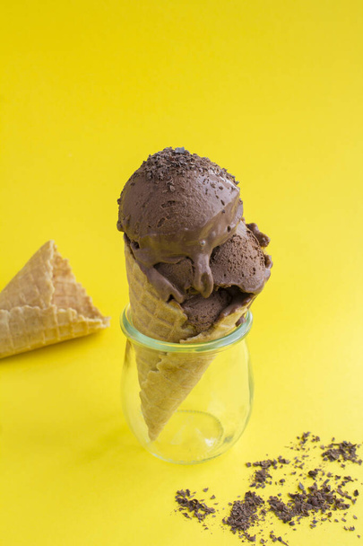 Csokis jégkrém gofris tölcsérben, sárga háttérrel. Függőleges elhelyezkedés. - Fotó, kép