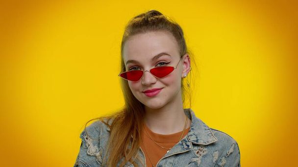 Verführerisch fröhlich stilvolles Mädchen in Jeansjacke mit Sonnenbrille, charmantes Lächeln an gelber Wand - Foto, Bild