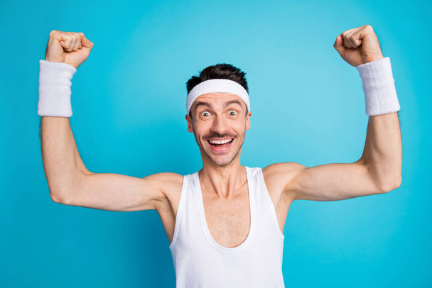 Photo of brunette happy man raise fists celebrate win wear sportswear headband isolated on blue color background - Fotó, kép
