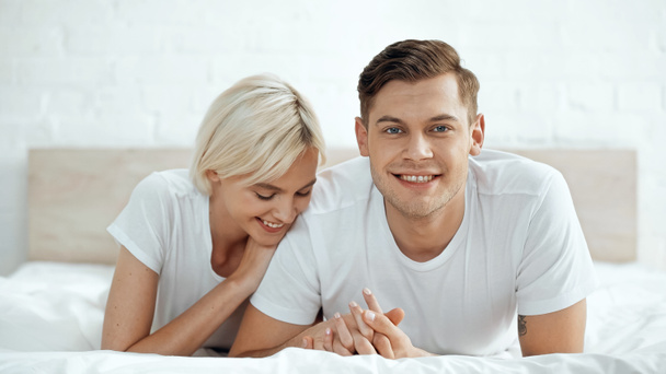 joyful man and cheerful woman holding hands on bed - Photo, image