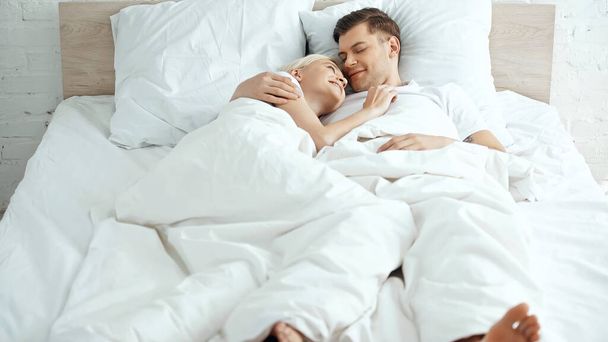 barefoot and happy couple lying under blanket on bed - Fotó, kép