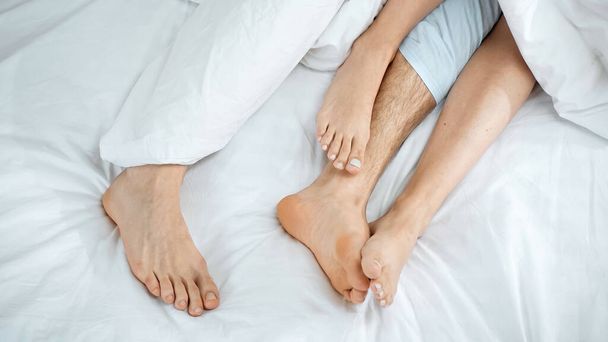 обрезанный вид босой пары лежащей на кровати - Фото, изображение