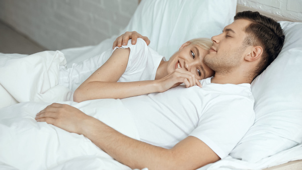 cheerful blonde woman resting in bed with boyfriend  - Zdjęcie, obraz