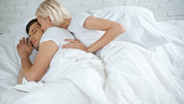young woman kissing young man sleeping in bed  - Фото, изображение