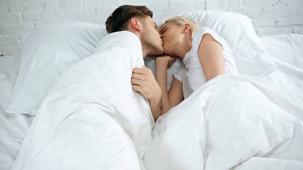 молодая женщина и мужчина целуются в постели  - Фото, изображение