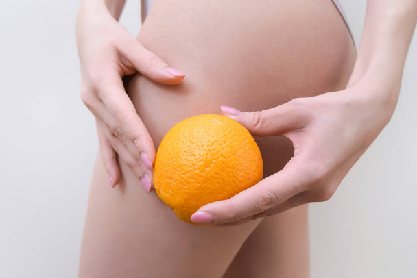 young woman is holding an orange on a light background. Cellulite problem concept - Zdjęcie, obraz