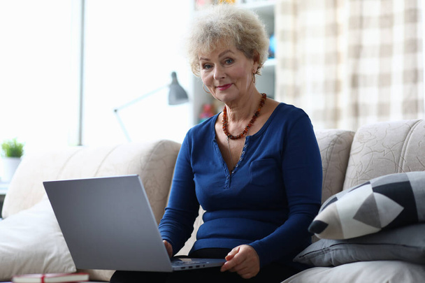 Elderly woman with laptop is sitting on couch - Photo, Image