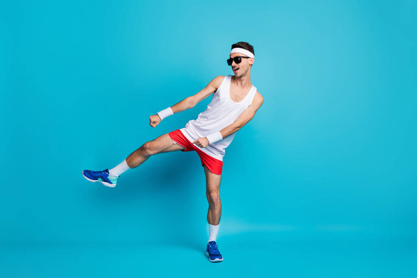 Teljes méretű fotó jóképű sportos férfi tánc funky viselet napszemüveg sportruházat elszigetelt kék színű háttér - Fotó, kép