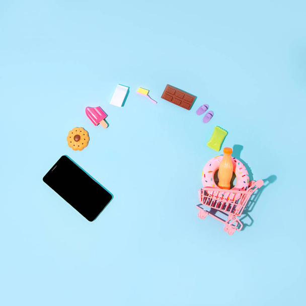 Buying things and food over the phone. Putting an item in the shopping cart. Advanced technology. Pastel blue background. - Foto, afbeelding