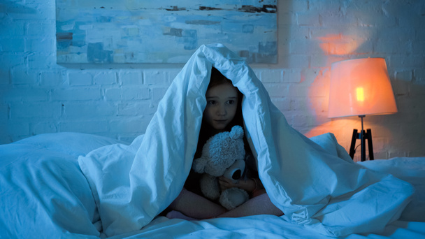 Lapsi, jolla on pehmeä lelu, kun hän istuu peiton alla sängyssä  - Valokuva, kuva