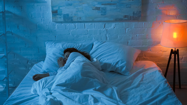 Lampadaire près de la femme dormant sur le lit pendant la nuit  - Photo, image
