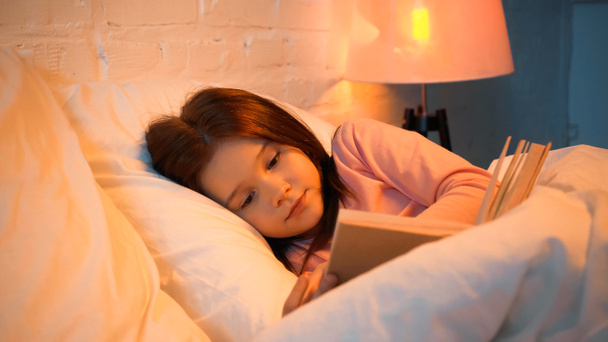 Παιδί ανάγνωση βιβλίο κοντά θολή κουβέρτα στο κρεβάτι  - Φωτογραφία, εικόνα
