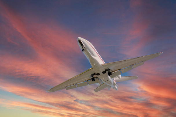 Airplane in the sky at sunrise or sunset. Small business jet is flying with lights and deployed landing gear preparing for landing or after takeoff - Photo, Image