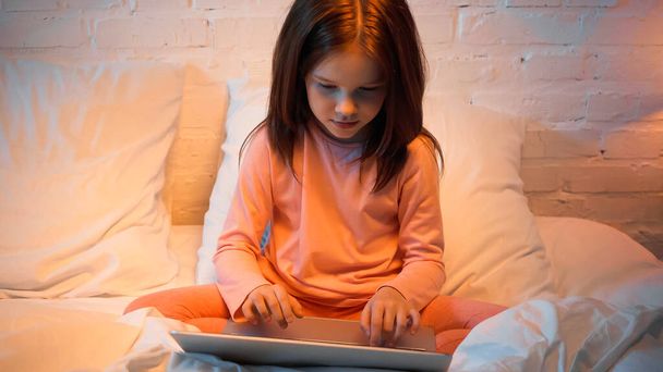 peuter kind met behulp van laptop terwijl zitten op bed  - Foto, afbeelding