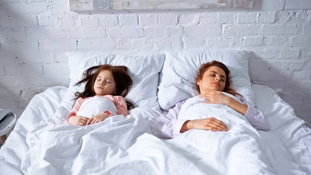 Mother and daughter sleeping on white bedding in morning  - Photo, image