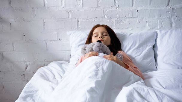 Preadolescent kind met zacht speelgoed slapen op bed  - Foto, afbeelding