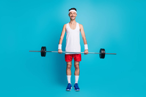 Full body photo of young sportsman happy smile lift barbell training bodybuilding isolated over blue color background - Zdjęcie, obraz