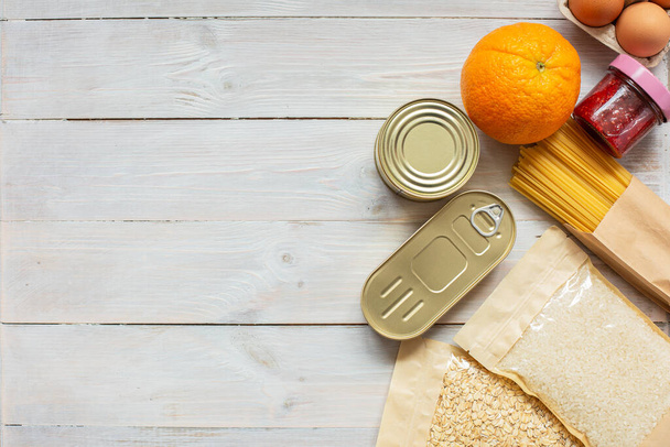 Donation food on wooden background with copy space. Flat lay. Mock up.Rice, canned, oat flakes, eggs, jam, pasta.Food donations or food delivery service concept.Online shopping during quarantine covid-1 - Foto, Imagem