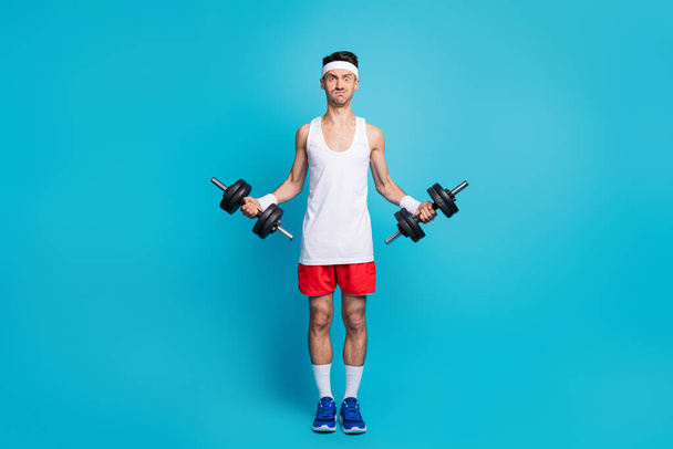 Full body photo of young man exercise dumbells biceps arms heavy difficult isolated over blue color background - Zdjęcie, obraz