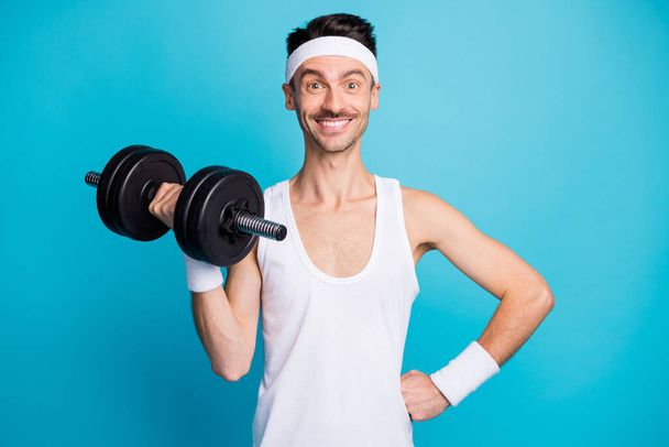 Portrait of cheerful handsome person put hand on waist lift dumbbell toothy smile isolated on blue color background - Фото, изображение