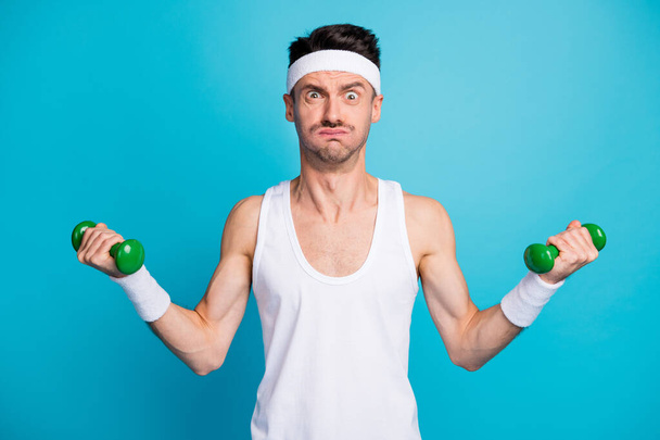Photo of young sportsman exercise with heavy dumbells pouted cheekbones grimacing isolated over blue color background - Φωτογραφία, εικόνα