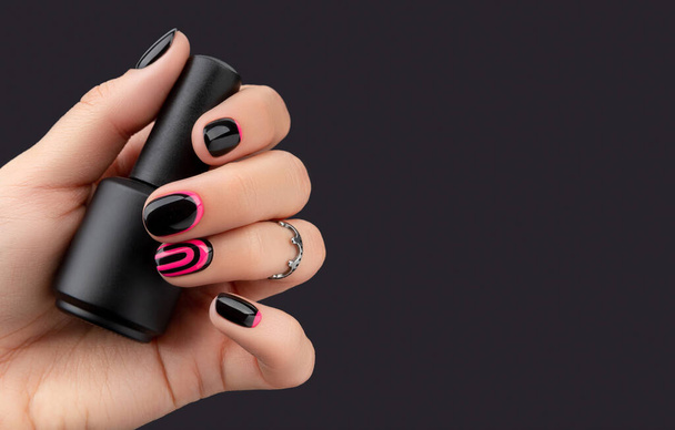 Vrouwen hand met trendy manicure houden nagel vernis op roze achtergrond - Foto, afbeelding