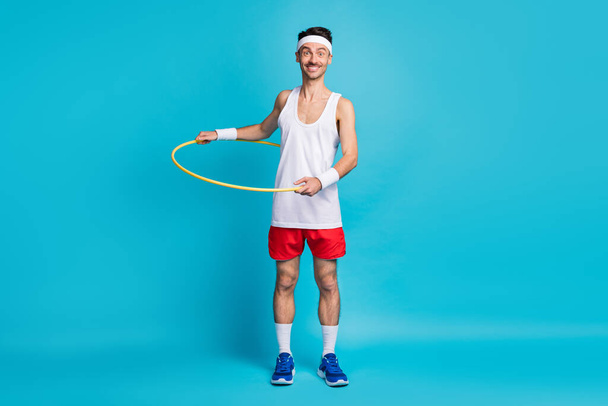 Photo of young excited man happy smile spin plastic circle around waist isolated over blue color background - Valokuva, kuva