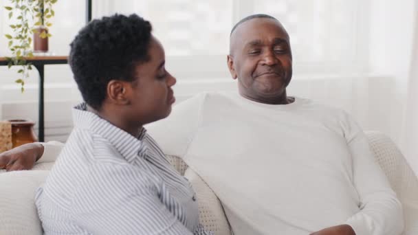 Conversación familiar en casa, afro-americano pareja marido y esposa hablando sentado en el sofá, negro étnico maduro de mediana edad hombre padre escuchando asiente cabeza entender y adulto africano mujer charlando - Imágenes, Vídeo