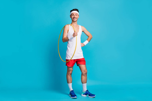 Full size portrait of cheerful man out hand on waist hold hula hoop beaming smile isolated on blue color background - Φωτογραφία, εικόνα