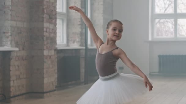 Retrato mediano de la linda bailarina de 9 años posando ante la cámara de pie en pose de ballet en la clase de baile con tutú blanco - Metraje, vídeo