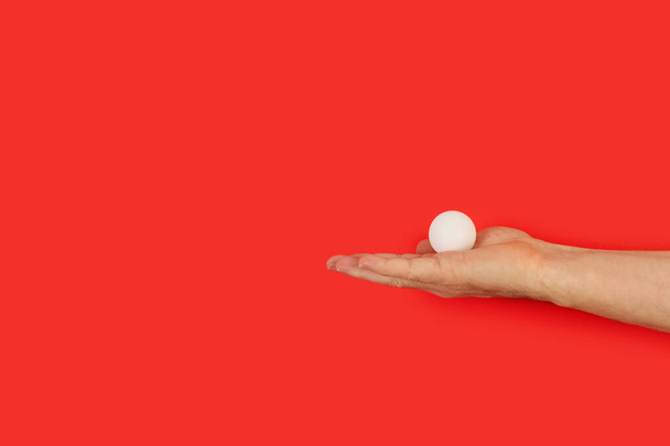 Mano de hombre sosteniendo una pelota de ping pong sobre un fondo rojo - Foto, imagen