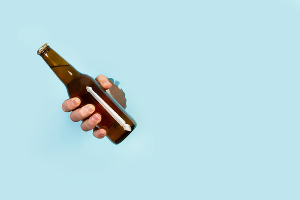 男の手は薄い青の背景に穴を通ってビールのボトルを保持 - 写真・画像