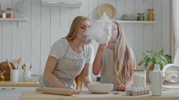 Caucasian family single mother mom with child teen girl daughter having fun in home kitchen play cooking blowing flour into air from iron sieve laugh entertainment at weekend cook food baking together - Footage, Video