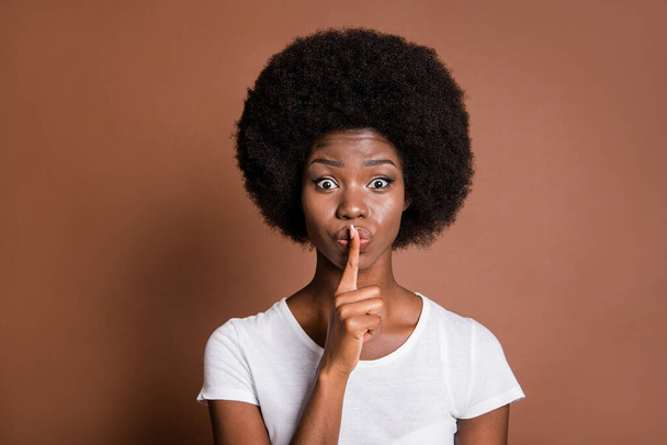 Photo portrait of girl touching lips with finger keeping secret speechless staring isolated on brown color background - Fotó, kép