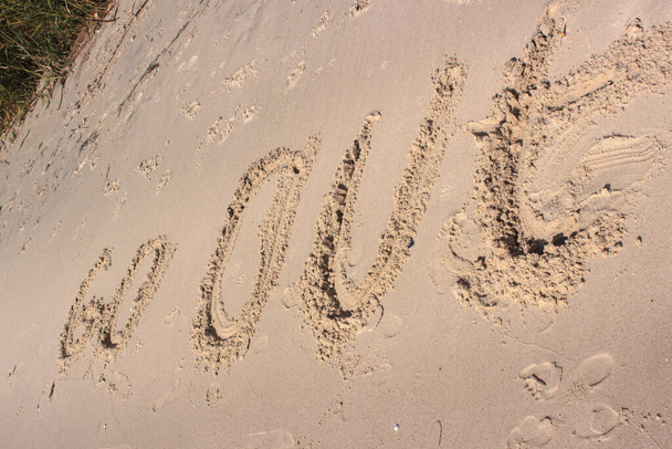Napis wykonywany jest na zdeptanym żółtym piasku morskim. "wyjdź". Napis jest zakrzywiony kulisto. Ślady gołych stóp są w pobliżu. Wezwanie do zakończenia kwarantanny - Zdjęcie, obraz